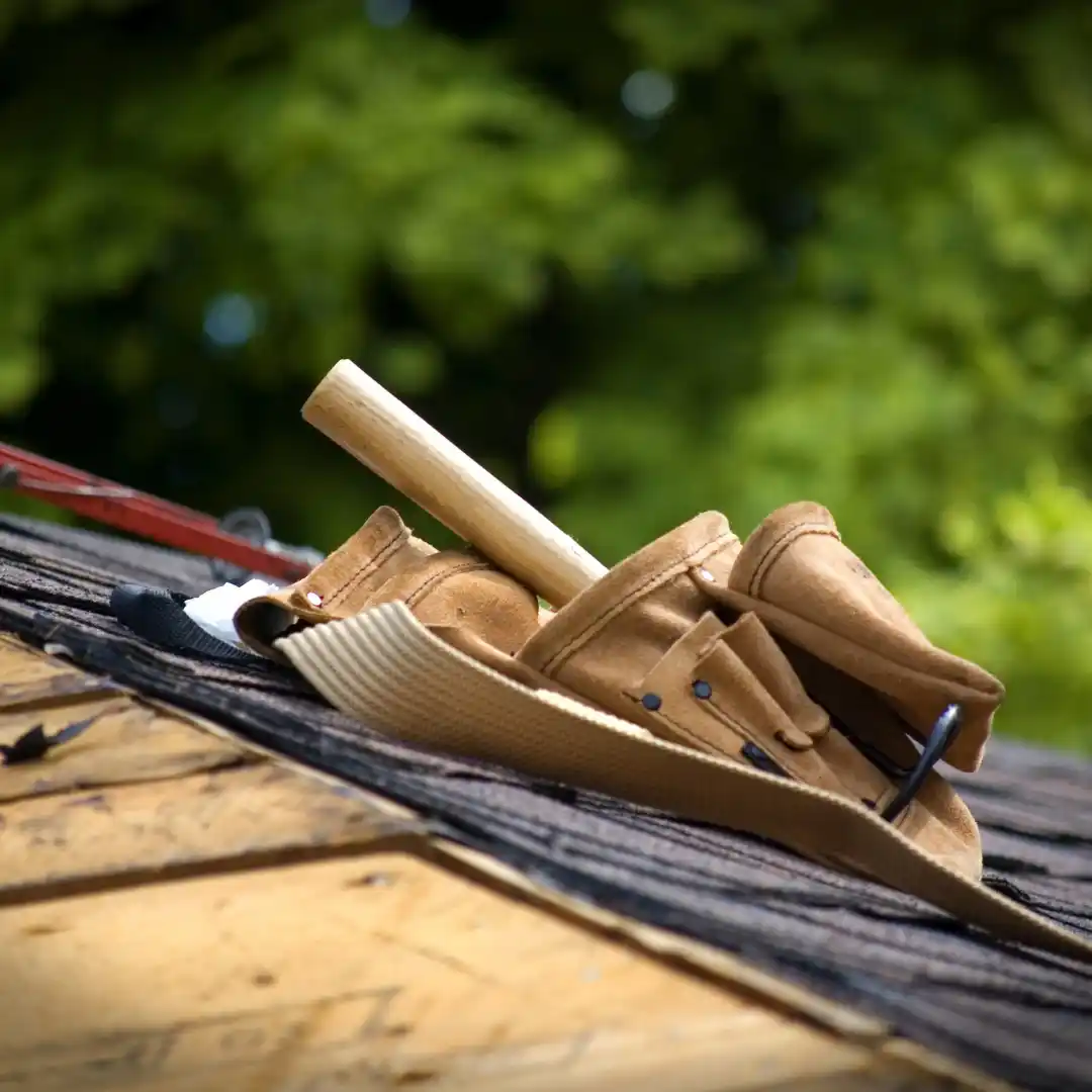 Tool bag with hammer sitting on shingle roof.